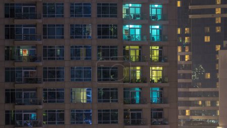Foto de Ventanas del edificio de varios pisos de iluminación de vidrio y acero en el interior y personas en movimiento dentro de timelapse. Vista aérea de los modernos rascacielos residenciales en Dubai marina
. - Imagen libre de derechos