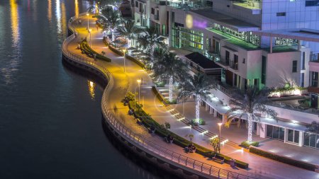 Téléchargez les photos : Bord de l'eau et promenade sur Dubai Marina skyline la nuit timelapse. Restaurants avec éclairage et éclairage. Yachts flottants et bateaux avec trafic près des gratte-ciel - en image libre de droit