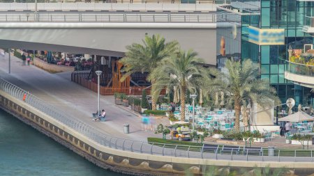 Téléchargez les photos : Promenade et canal à Dubai Marina avec des gratte-ciel de luxe et des yachts autour de timelapse, Émirats arabes unis. Vue aérienne avec restaurants et cafés près du pont - en image libre de droit