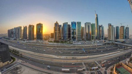 Foto de Panorama aéreo de Jumeirah lagos torres rascacielos al amanecer timelapse con el tráfico en sheikh zayed carretera y línea de metro. Vista desde el puerto deportivo de Dubái - Imagen libre de derechos