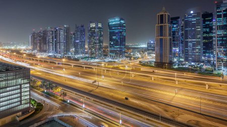 Téléchargez les photos : Vue aérienne des tours des lacs Jumeirah avec des gratte-ciel éclairés timelapse de nuit avec la circulation sur la route cheikh zayed et la ligne de métro. Vue sur le toit depuis la marina de Dubaï - en image libre de droit