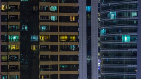 Téléchargez les photos : Fenêtres du bâtiment de plusieurs étages d'éclairage en verre et en acier à l'intérieur et les personnes en mouvement dans le temps. Vue aérienne des gratte-ciel résidentiels et de bureaux modernes à Dubaï
. - en image libre de droit