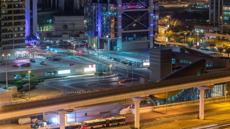Téléchargez les photos : Vue aérienne des tours des lacs Jumeirah avec des gratte-ciel éclairés nuit avec parking et la circulation sur la route cheikh zayed et la ligne de métro. Bus près de la sortie de la station de métro. Marina de Dubai sur le toit - en image libre de droit