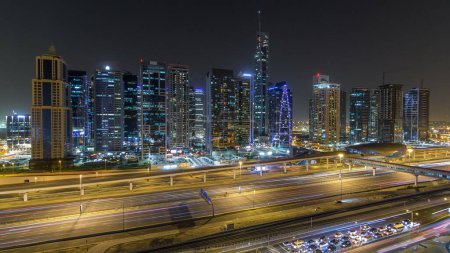 Foto de Vista aérea de las torres de los lagos Jumeirah con rascacielos iluminados timelapse noche con el tráfico en la intersección cerca de Sheikh zayed carretera y línea de metro. Vista desde el puerto deportivo de Dubái - Imagen libre de derechos
