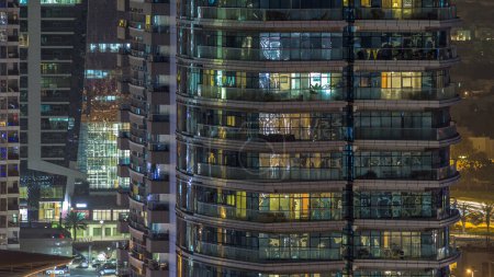 Foto de Ventanas del edificio de varios pisos de iluminación de vidrio y acero en el interior y personas en movimiento dentro de timelapse. Vista aérea de los modernos rascacielos residenciales y de oficinas en Dubai marina
. - Imagen libre de derechos