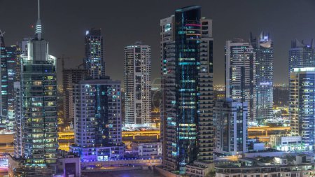 Foto de Torres residenciales con iluminación y timelapse de iluminación. Carretera y paseo marítimo en Dubai Marina y JLT skyline por la noche. Tráfico cerca de rascacielos con ventanas brillantes - Imagen libre de derechos