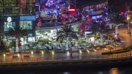 Téléchargez les photos : Promenade et canal à Dubai Marina avec des bâtiments de luxe et des yachts autour de la nuit timelapse, Émirats arabes unis. Vue aérienne avec restaurants et cafés sur la passerelle - en image libre de droit