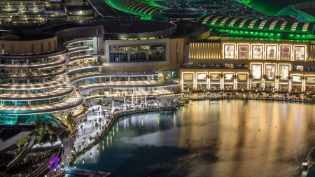 Téléchargez les photos : Vue aérienne de nuit Fontaines dansantes au centre-ville et dans un timelapse de lac artificiel à Dubaï, Émirats arabes unis. Bâtiments éclairés. De nombreux téléspectateurs sur le front de mer - en image libre de droit