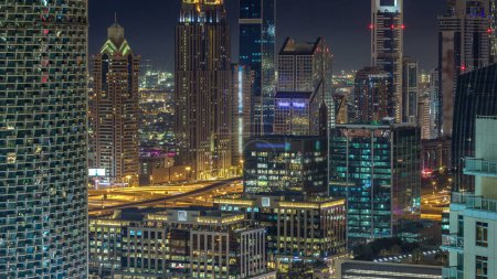 Foto de Dubai timelapse noche céntrica, edificios modernos de lujo iluminados en camino sheikh zayed, paisaje urbano futurista de Emiratos Árabes Unidos. Vista aérea del distrito financiero desde el rascacielos - Imagen libre de derechos