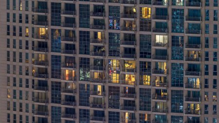 Téléchargez les photos : Fenêtres du bâtiment de plusieurs étages d'éclairage en verre et en acier à l'intérieur et les personnes en mouvement dans le temps. Vue aérienne des gratte-ciel résidentiels modernes du centre-ville de Dubaï - en image libre de droit