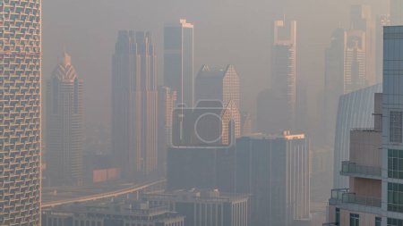 Foto de Mañana brumosa en el centro de Dubai timelapse. Vista futurista de los rascacielos de la ciudad en el distrito financiero cubierto de niebla. Vista aérea desde la azotea con torres modernas durante el amanecer. Dubai, Emiratos Árabes Unidos - Imagen libre de derechos