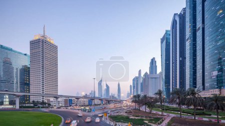 Téléchargez les photos : Trafic sur l'intersection et le pont à la route Sheikh Zayed entouré de gratte-ciel jour à nuit passage timelapse. Vue panoramique d'en haut à Dubaï le soir, Émirats arabes unis - en image libre de droit