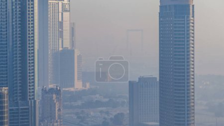 Foto de Mañana brumosa en el centro de Dubai timelapse. Vista futurista de los rascacielos de la ciudad cubiertos de niebla. Vista aérea desde la azotea con modernas torres cerca del distrito de Zabeel durante el amanecer. Dubai, Emiratos Árabes Unidos - Imagen libre de derechos