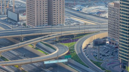 Téléchargez les photos : Trafic sur une intersection achalandée sur l'autoroute Cheikh Zayed timelapse aérien. Site de construction de l'arène sur un fond. Vue depuis le toit du gratte-ciel à la soirée ensoleillée avant le coucher du soleil - en image libre de droit