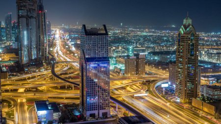 Tráfico nocturno en una concurrida intersección en el timelapse aéreo de la autopista Sheikh Zayed. Vista desde la azotea en el centro de Dubai con rascacielos modernos

