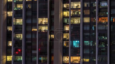 Téléchargez les photos : Fenêtres du bâtiment de plusieurs étages d'éclairage en verre et en acier à l'intérieur et les personnes en mouvement dans le temps. Vue aérienne des gratte-ciel résidentiels modernes du centre-ville de Dubaï - en image libre de droit