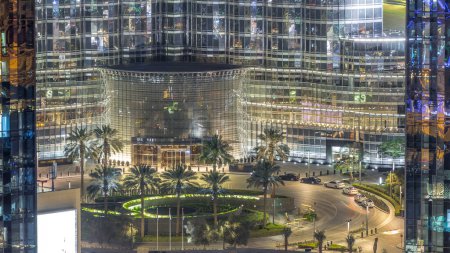 Téléchargez les photos : Dubaï nuit au centre-ville, éclairé bâtiments modernes de luxe et fontaine avec la circulation sur le cercle près de l'entrée du plus haut bâtiment, paysage urbain des Émirats arabes unis. Vue aérienne du dessus depuis le gratte-ciel - en image libre de droit
