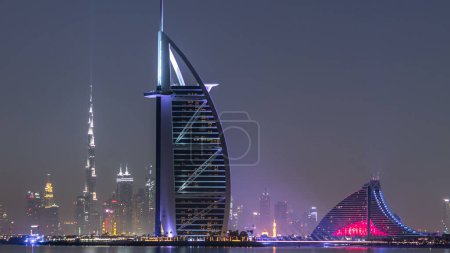 Téléchargez les photos : Skyline de Dubaï la nuit avec Burj Al Arab de la Palm Jumeirah timelapse. gratte-ciel éclairés réfléchis dans l'eau - en image libre de droit