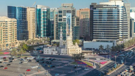 Photo for Mosque near Dubai Creek surrounded by modern buildings and busy traffic street timelapse. Aerial top view from above at sunset with long shadows - Royalty Free Image