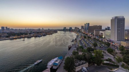 Téléchargez les photos : Dubaï crique paysage panoramique jour à nuit transition timelapse avec des bateaux et des yachts et des bâtiments modernes avec circulation sur la route et un parking. Vue aérienne du dessus d'en haut - en image libre de droit