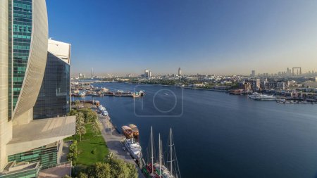 Téléchargez les photos : Dubaï Creek paysage panoramique timelapse avec des bateaux et des navires dans le port, l'eau calme et des bâtiments modernes en arrière-plan pendant le coucher du soleil. Vue aérienne du dessus d'en haut - en image libre de droit
