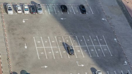 Photo for Top view of parking lot timelapse from rooftop of skyscraper, with varieties of colored vehicles such as yellow, white, black, grey, silver, blue and other. Cars changes, shadows moves fast. Dubai, UAE - Royalty Free Image