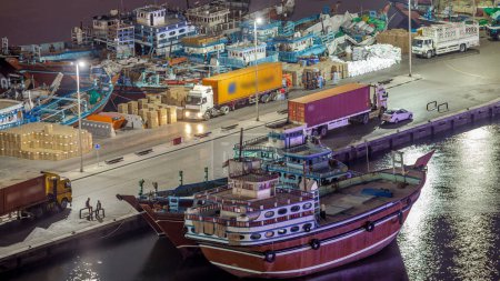 Téléchargez les photos : Chargement d'un navire à Port Saïd timelapse nocturne à Dubaï, Deira creek, EAU. Vue aérienne rapprochée d'en haut avec de nombreux vieux bateaux et lampadaires - en image libre de droit