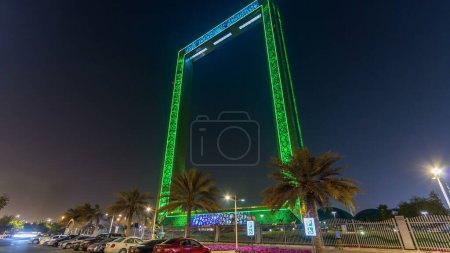 Téléchargez les photos : Dubaï Bâtiment de cadre la nuit timelapse avec éclairage, nouvelle attraction des EAU. Vue depuis le parking avec palmiers. Le cadre mesure 150 mètres de haut et 93 mètres de large et sa nouvelle attraction Dubaï - en image libre de droit