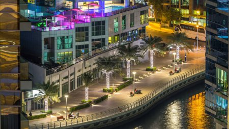 Téléchargez les photos : Vue aérienne du port de plaisance de Dubaï d'un point de vue timelapse de nuit. Les gens marchent sur la promenade au bord de l'eau. gratte-ciel et tours résidentielles modernes éclairés par des fenêtres éclatantes - en image libre de droit