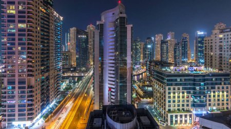 Téléchargez les photos : Vue panoramique aérienne de la marina de Dubaï à partir d'un point de vue timelapse de nuit. Des gratte-ciels modernes et des tours résidentielles éclairées par des fenêtres éclatantes. Trafic sur la route - en image libre de droit