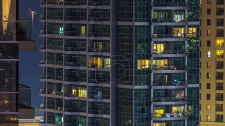 Photo for Glowing windows in multistory modern glass and metal residential building light up at night timelapse. People in apartments. Houses illuminated at night. Dubai Marina and JBR, UAE - Royalty Free Image
