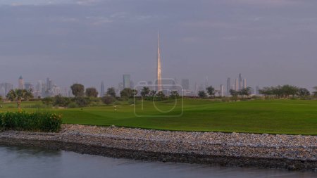 wunderschöner Golfplatz bei Sonnenaufgang rund um moderne Wolkenkratzer der Dubaier Innenstadt im Zeitraffer in der luxuriösen Dubaier Stadt, vereinigte arabische Emirate. Grüner Rasen, Teich und bewölkter Himmel