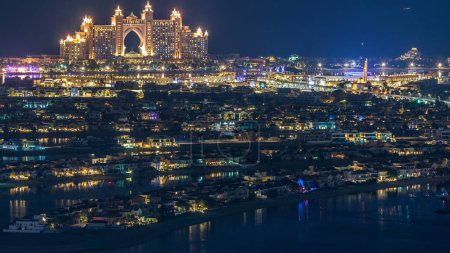 Téléchargez les photos : Vue aérienne du timelapse nocturne de Palm Jumeirah Island. Vue de dessus avec villas éclairées, hôtels et yachts. Monorail se déplaçant à droite - en image libre de droit