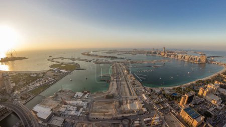 Photo for Aerial sunset view of Palm Jumeirah Island day to night transition timelapse. Evening top view with illuminated villas, hotels and yachts. Construction process of new cruise terminal - Royalty Free Image