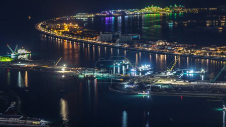 Téléchargez les photos : Vue aérienne du timelapse nocturne de Palm Jumeirah Island. Vue de dessus avec villas, hôtels et yachts. Processus de construction du nouveau terminal de croisière - en image libre de droit