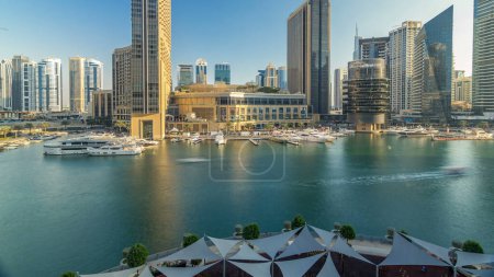Foto de Vista aérea de Dubai Marina con centro comercial, restaurantes, torres y yates timelapse, Emiratos Árabes Unidos. Vista superior del canal por la noche antes del atardecer - Imagen libre de derechos