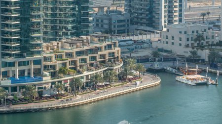 Téléchargez les photos : Luxe canal Marina de Dubaï avec des bateaux de passage et promenade avec palmiers timelapse, vue de dessus le soir avant le coucher du soleil. Dubai, Émirats arabes unis - en image libre de droit
