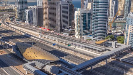 Foto de Edificio futurista de la estación de metro y tranvía de Dubái y rascacielos de lujo detrás de timelapse en Dubai Marina, Emiratos Árabes Unidos. Vista aérea desde JLT con tráfico en la carretera sheikh zayed - Imagen libre de derechos