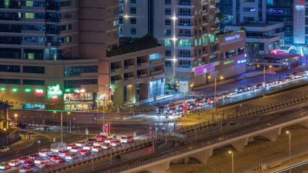 Téléchargez les photos : Vue aérienne d'une intersection routière dans une grande ville timelapse nocturne. Paysage urbain du quartier Marina de Dubaï aux EAU avec voitures et tramway - en image libre de droit