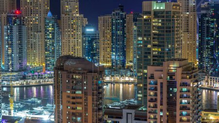 Foto de Fantástico horizonte en la azotea del puerto deportivo de Dubai con timelapse barcos. Rascacielos iluminados de una gran ciudad por la noche, Emiratos Árabes Unidos. Vista aérea desde JLT - Imagen libre de derechos
