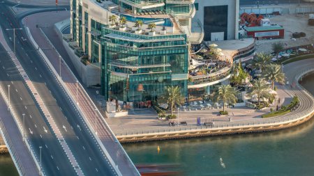 Téléchargez les photos : Canal de luxe de Dubai Marina et promenade avec palmiers et cafés timelapse, la circulation sur le pont. Vue de dessus le soir avant le coucher du soleil. Dubai, Émirats arabes unis - en image libre de droit