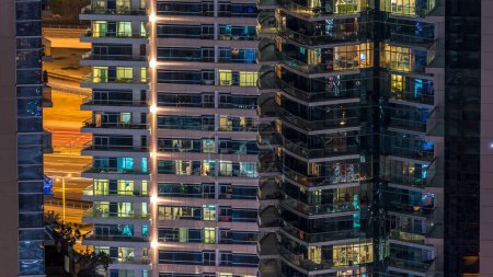 Téléchargez les photos : Des fenêtres éclatantes dans un immeuble résidentiel moderne à plusieurs étages en verre et en métal s'illuminent la nuit. Des gens dans des appartements. Maisons éclairées la nuit. Dubai, Émirats arabes unis - en image libre de droit
