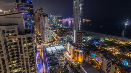 Téléchargez les photos : Vue aérienne des gratte-ciel et de la plage éclairés modernes de la résidence Jumeirah Beach Residence (JBR), à Dubaï, Émirats arabes unis. Bateaux et yachts flottant sur l'eau du Golfe - en image libre de droit
