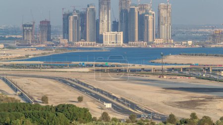 Foto de Construcción de nuevos rascacielos en Dubai Creek Harbor timelapse aéreo. Dubai - EAU. Vista superior desde el centro de Dubái con tráfico en una autopista - Imagen libre de derechos