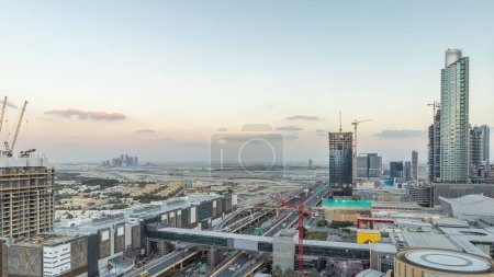Téléchargez les photos : Vue aérienne du centre financier route de jour à la nuit transition timelapse avec centre commercial et en construction bâtiment avec grues du centre-ville, Dubai Creek port sur fond - en image libre de droit