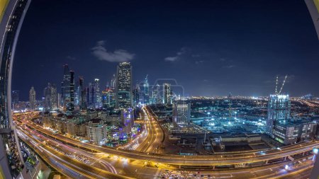 Foto de Rascacielos vista panorámica aérea en el centro y el distrito financiero Dubai noche timelapse, el tráfico en las carreteras. Emiratos Árabes Unidos con torres iluminadas y cielo nublado - Imagen libre de derechos