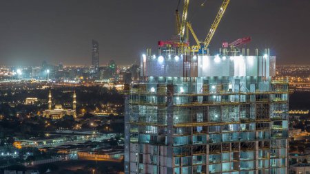 Téléchargez les photos : Activité de construction au centre-ville de Dubaï avec grues et travailleurs nuit timelapse, Émirats arabes unis. Construction de nouveaux gratte-ciel et tours - en image libre de droit