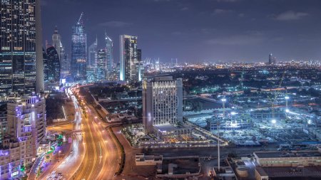 Foto de Actividad de construcción en el centro de Dubái con grúas y timelapse de tráfico nocturno, EAU. Construcción de nuevos rascacielos y torres cerca de la intersección de la calle Al Saada y la carretera del centro financiero - Imagen libre de derechos