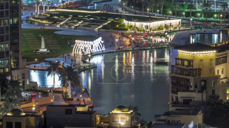 Téléchargez les photos : Top vue rapprochée du pont sur le lac artificiel et certaines personnes marchant dans le parc avec monument à la main timelapse nuit dans le centre de Dubaï, Émirats arabes unis
. - en image libre de droit