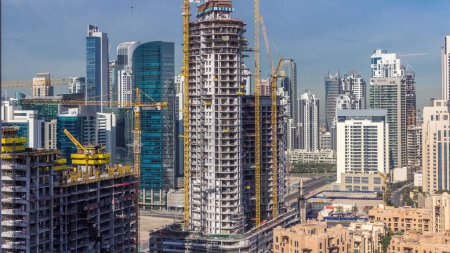 Foto de Actividad de construcción en el centro de Dubai con grúas y timelapse de trabajadores, Emiratos Árabes Unidos. Construcción de nuevos rascacielos y torres cerca de la bahía de negocios - Imagen libre de derechos